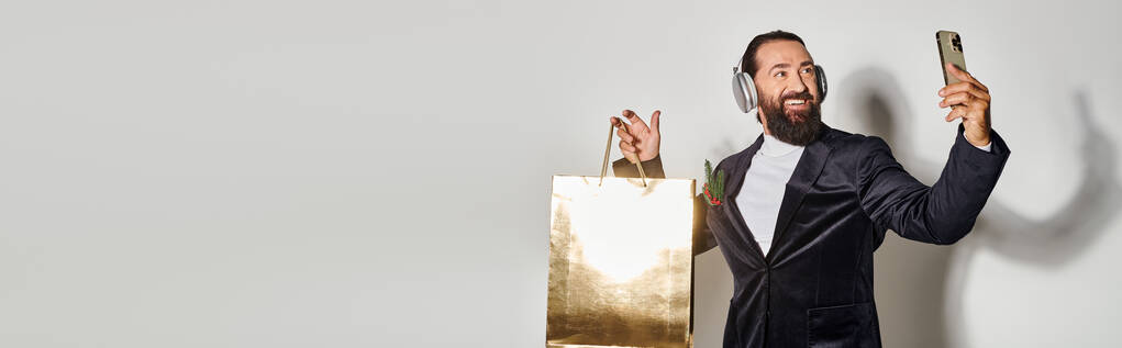 ハッピーベアード男 ヘッドフォンでセルフィーを取る スマートフォンやグレーのショッピングバッグ, バナー - 写真・画像