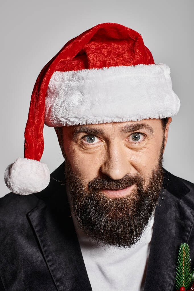 portrait de bel homme barbu en costume élégant et chapeau de Père Noël posant sur fond gris, Noël - Photo, image