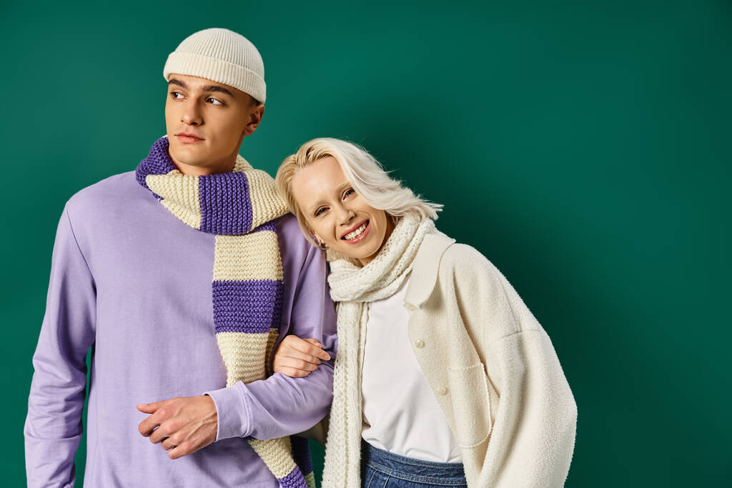 pareja en traje de invierno, mujer feliz apoyándose en el hombre con ropa elegante sobre fondo turquesa - Foto, imagen