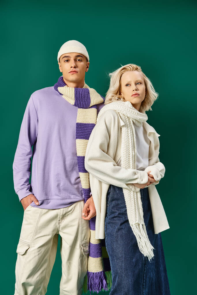ζευγάρι με χειμωνιάτικα ρούχα, ξανθιά γυναίκα που ποζάρει με άντρα με μοντέρνα ρούχα σε τυρκουάζ φόντο - Φωτογραφία, εικόνα