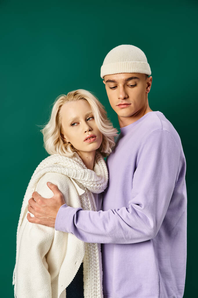 lange knappe man in beanie hoed omarmen blonde vrouw in de winter kleding op turquoise achtergrond - Foto, afbeelding