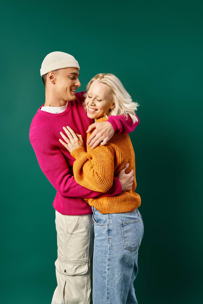 Paar in Winterkleidung, Mann in Mütze umarmt glückliche Freundin auf Türkis, Wintermode - Foto, Bild