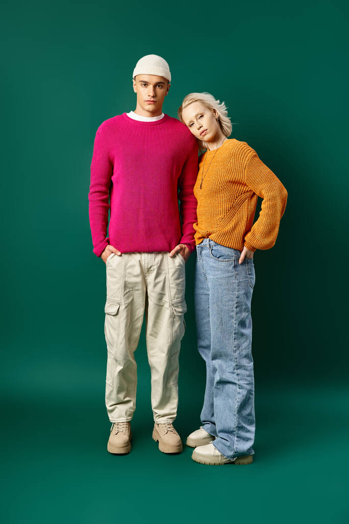 stylish couple in fashionable outfits posing with hands in pockets on turquoise background - Photo, Image