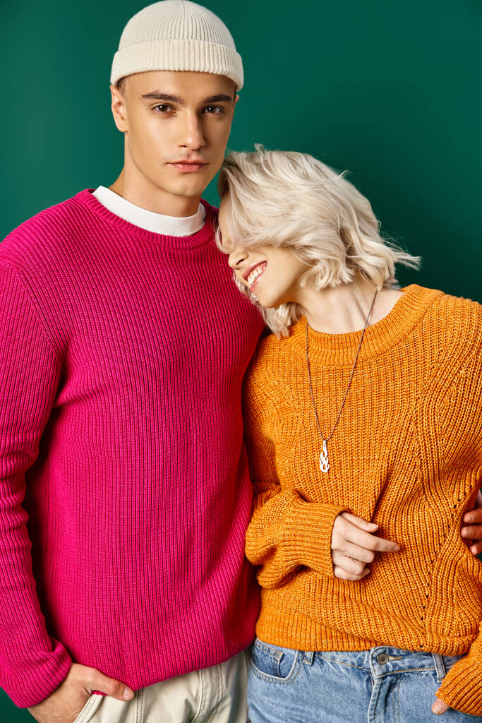 happy blonde woman leaning on handsome boyfriend in sweater on turquoise background, young couple - Photo, Image