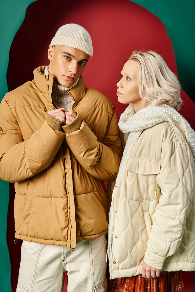 冬のジャケットで若い金髪の女性とターコイズの背景で赤い男性を見たニットスカーフ - 写真・画像
