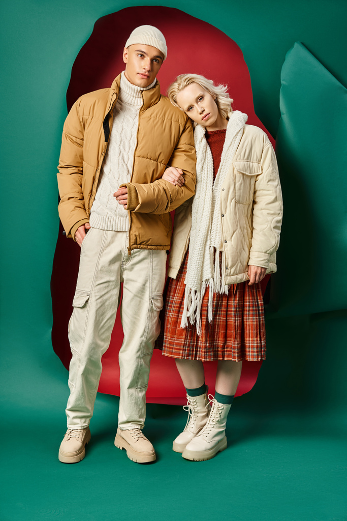 plná délka mladých párů v zimních bundách pózujících společně na červené s tyrkysovým pozadím - Fotografie, Obrázek