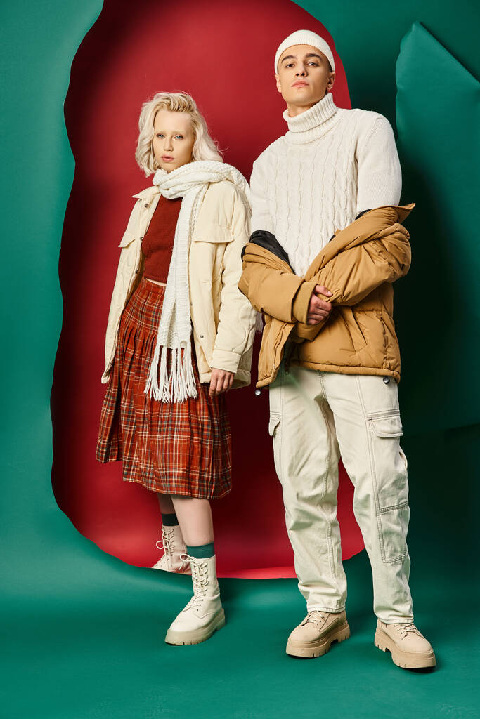 piena lunghezza di bell'uomo in abbigliamento invernale alla moda posa vicino alla donna sul rosso con sfondo turchese - Foto, immagini