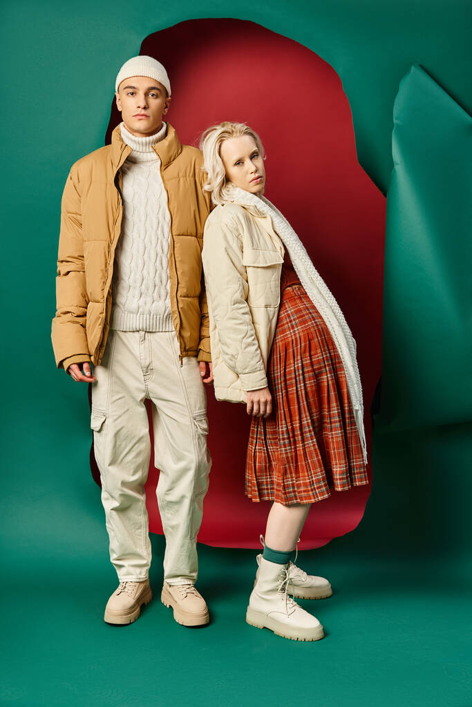 pełna długość pary w modnych kurtkach zimowych pozowanie razem na czerwono z turkusowym tle - Zdjęcie, obraz