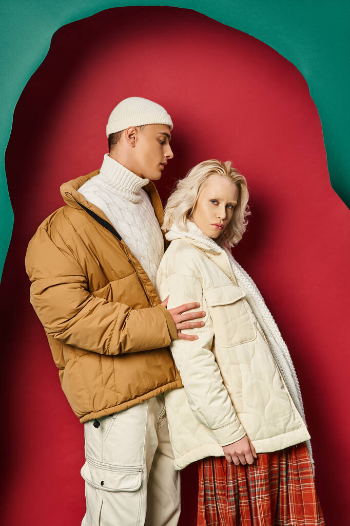 joven hombre y mujer con elegantes chaquetas de invierno posando juntos sobre un fondo rojo y turquesa desgarrado - Foto, Imagen