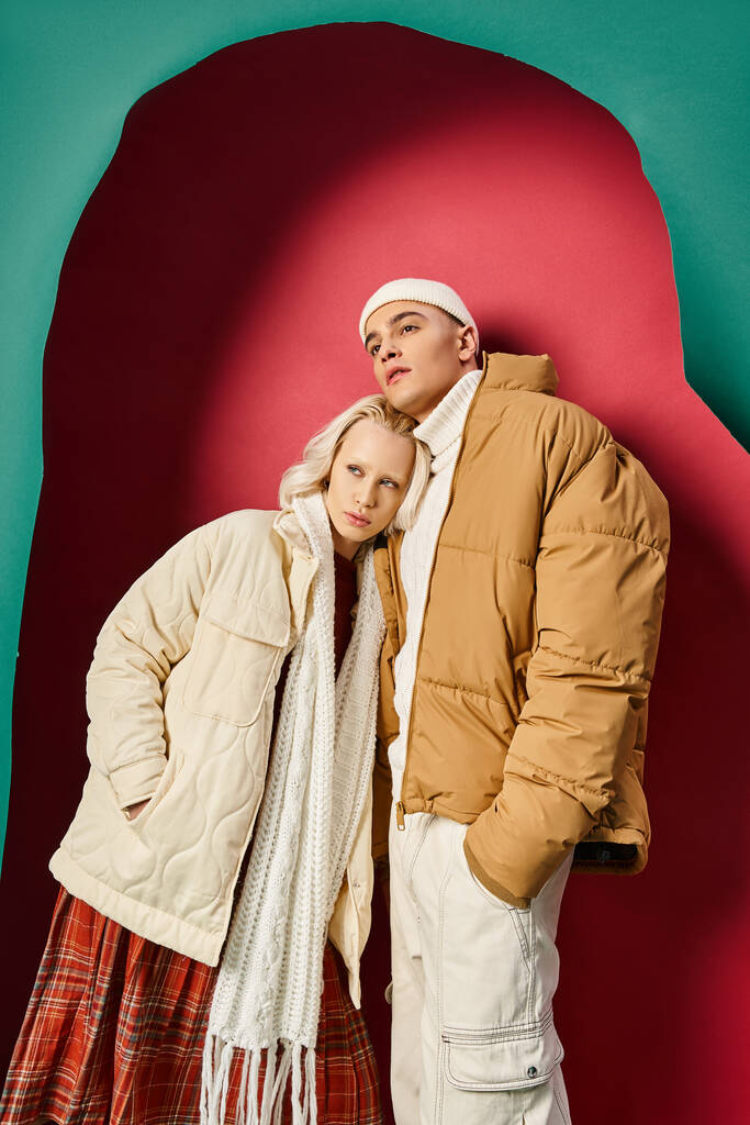 junges romantisches Paar in winterlichen Outfits vor zerrissenem türkis-rotem Hintergrund - Foto, Bild
