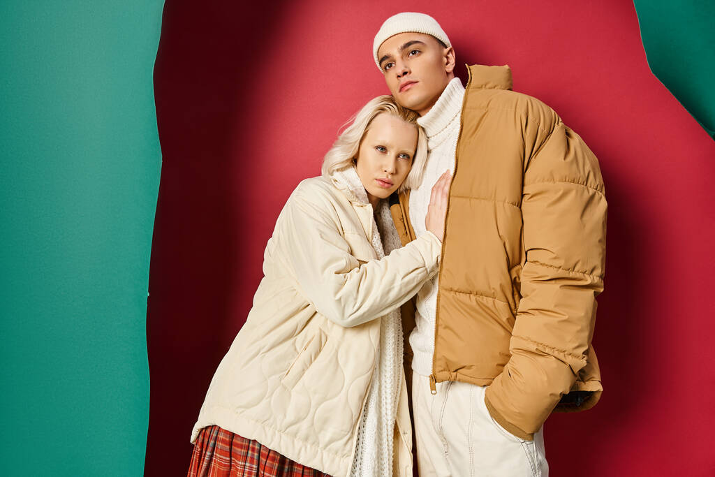 mladý romantický pár v zimních bundách stojící vedle sebe v blízkosti roztržené tyrkysové a červené pozadí - Fotografie, Obrázek