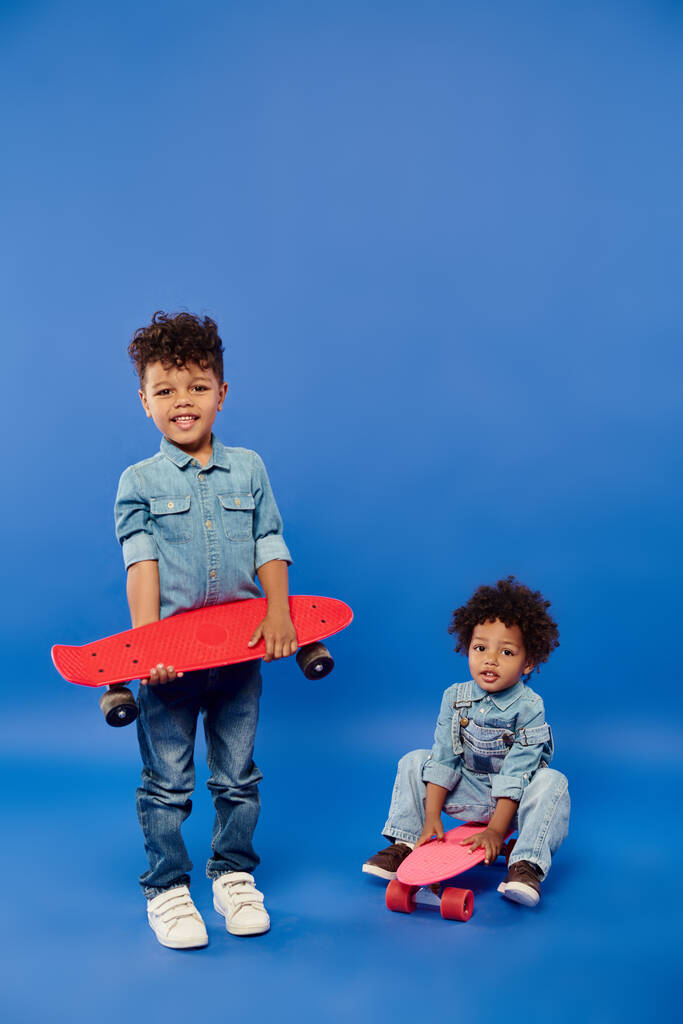 cute african american siblings in stylish denim clothes with penny boards on blue backdrop - Photo, Image