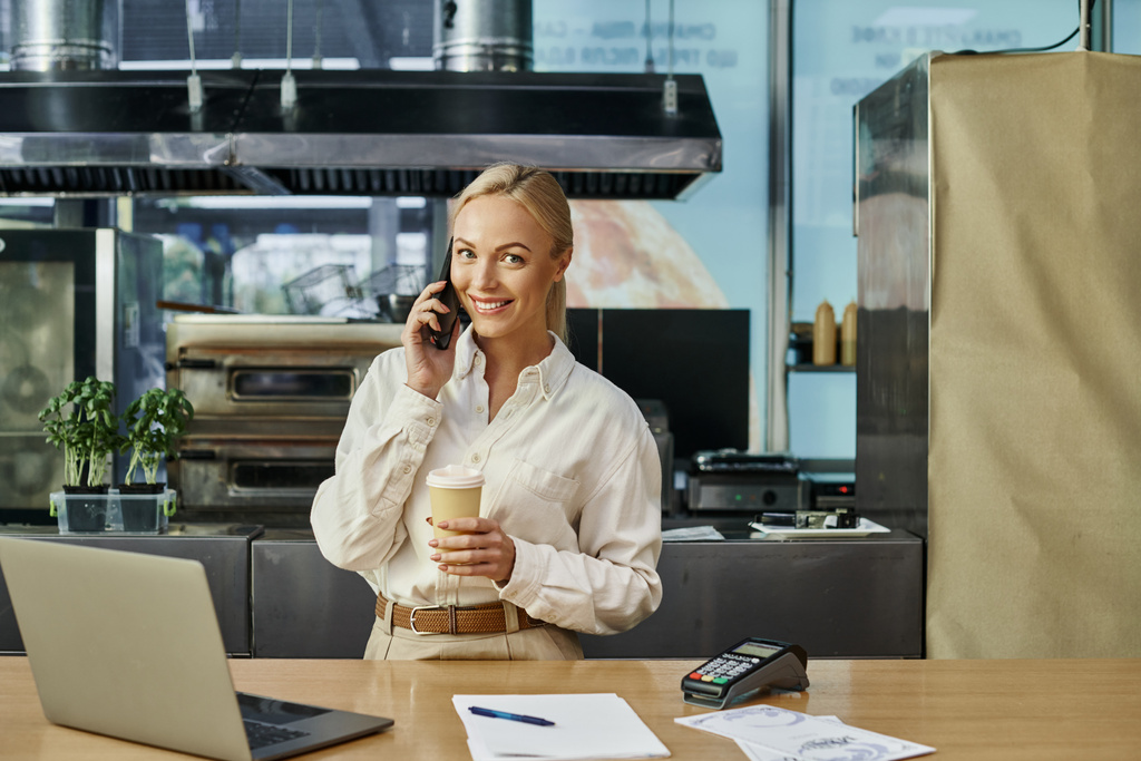 щасливий адміністратор кафе з кавою, щоб піти говорити по смартфонах біля ноутбука і платіжного терміналу - Фото, зображення