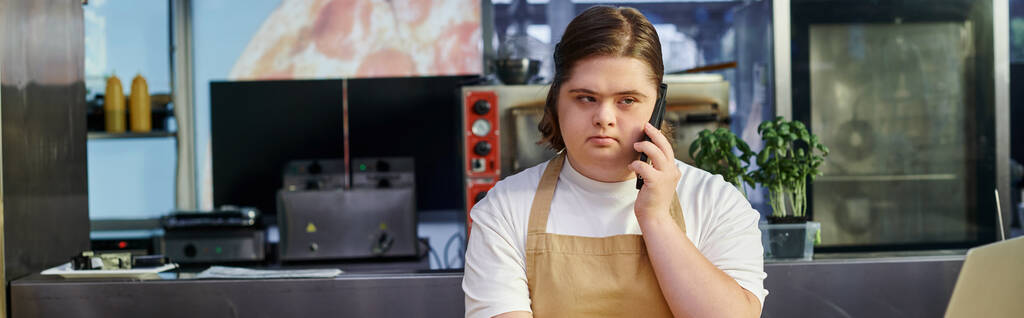 mujer joven con síndrome de Down hablando por teléfono móvil mientras trabaja en la cafetería moderna, pancarta - Foto, imagen