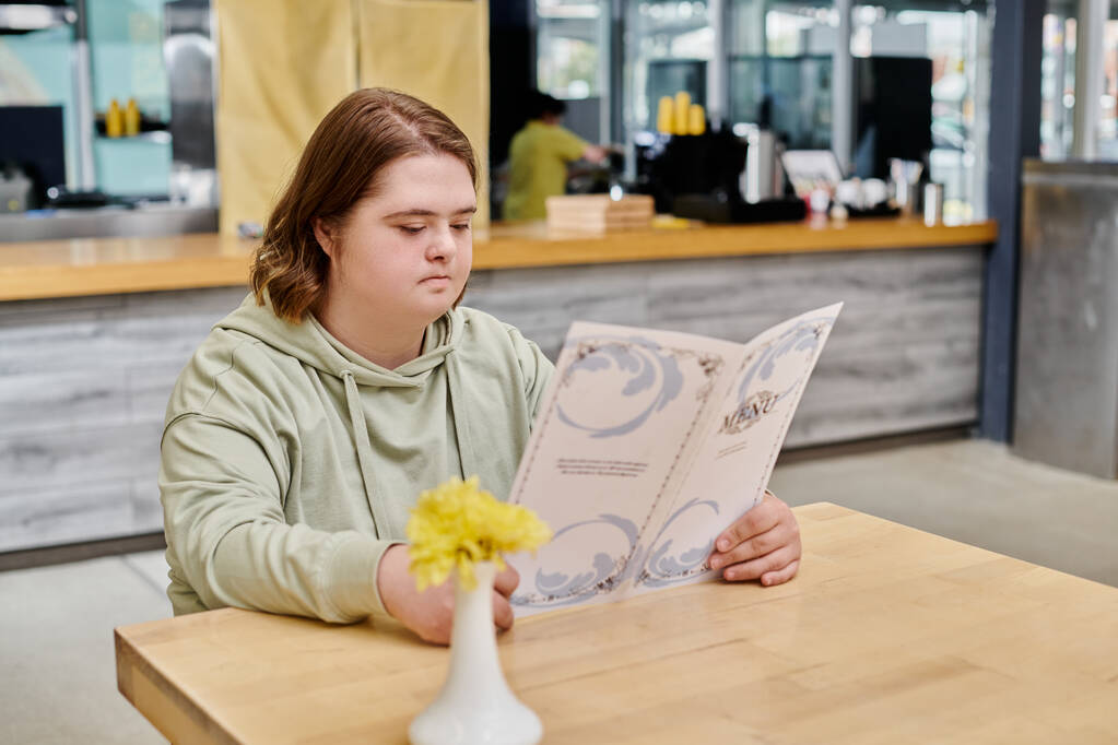 вдумчивая клиентка с синдромом Дауна, смотрящая на карту меню, сидя за столом в кафе - Фото, изображение