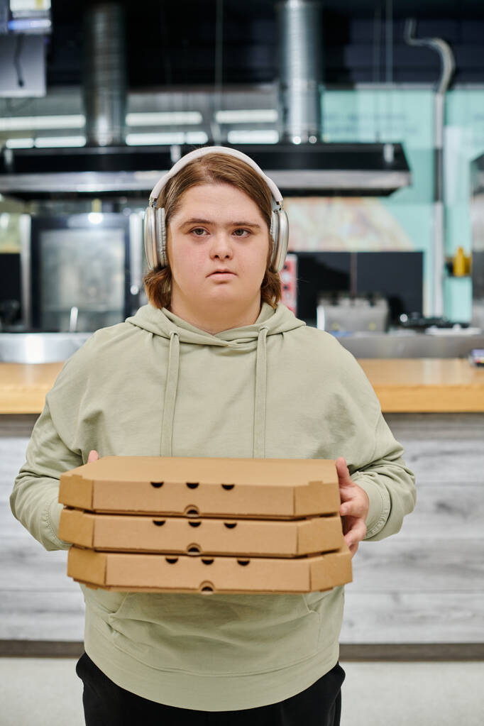 młoda kobieta z zaburzeniami psychicznymi w słuchawkach bezprzewodowych trzymając pudełka pizzy w nowoczesnej kawiarni - Zdjęcie, obraz