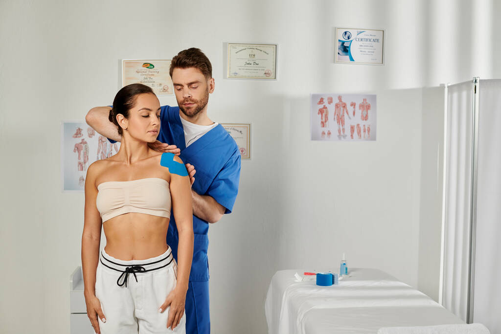 dobře vypadající lékař dává kineziologické pásky na rameno svého mladého pacienta, zdravotní péče - Fotografie, Obrázek