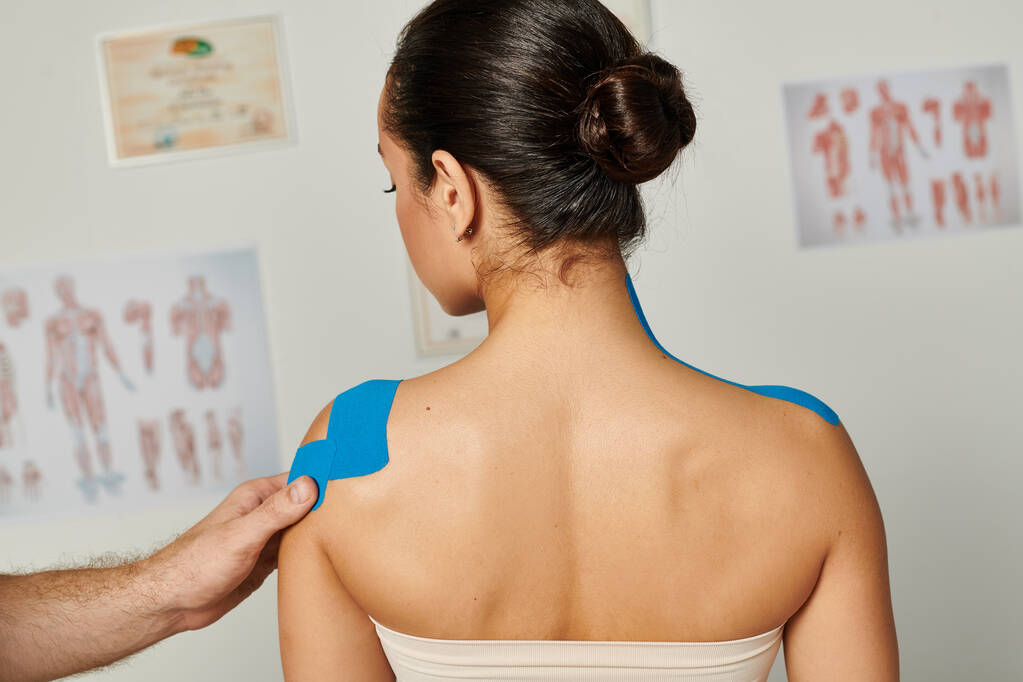 vista recortada del médico poniendo cintas cinesiológicas en el hombro de una joven mujer atractiva paciente - Foto, imagen
