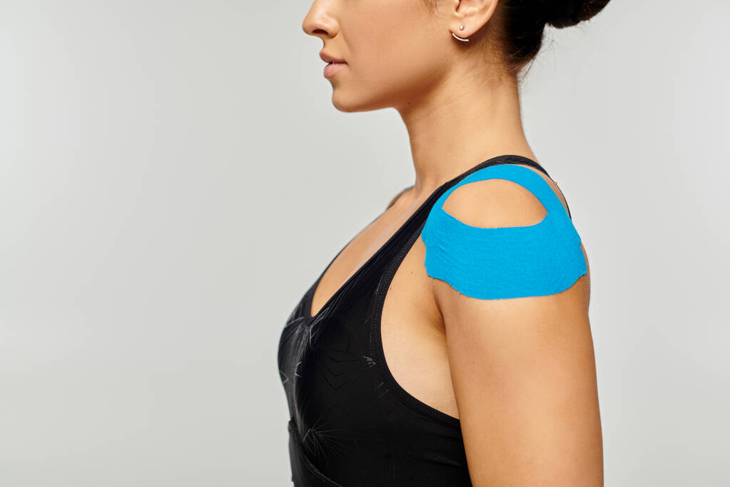 abgeschnittene Ansicht einer jungen Frau in Sportkleidung, die im Profil mit kinesiologischen Bändern auf der Schulter posiert - Foto, Bild