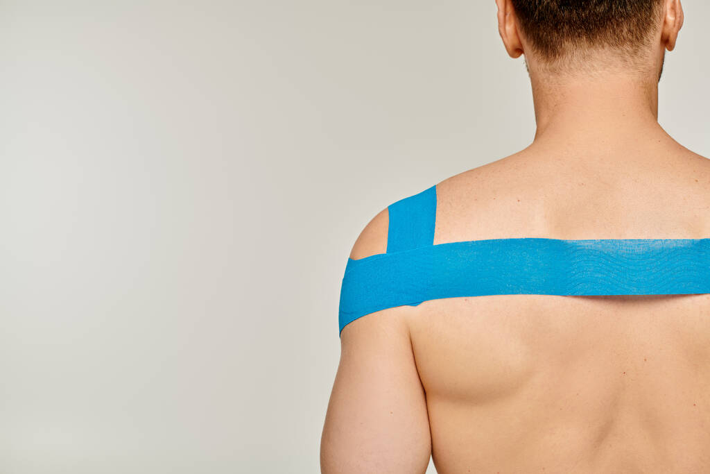 achteraanzicht van sportief mannelijk model met kinesiologische banden op zijn schouder en rug op grijze achtergrond - Foto, afbeelding