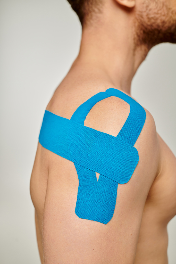 vista recortada del hombre con cintas cinesiológicas azules en su hombro y espalda sobre fondo gris - Foto, Imagen