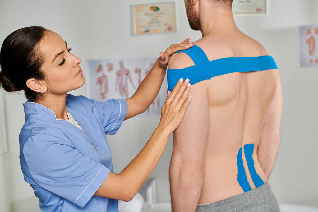 attractive young doctor putting kinesiological tapes on her bearded male patient, healthcare - Photo, Image