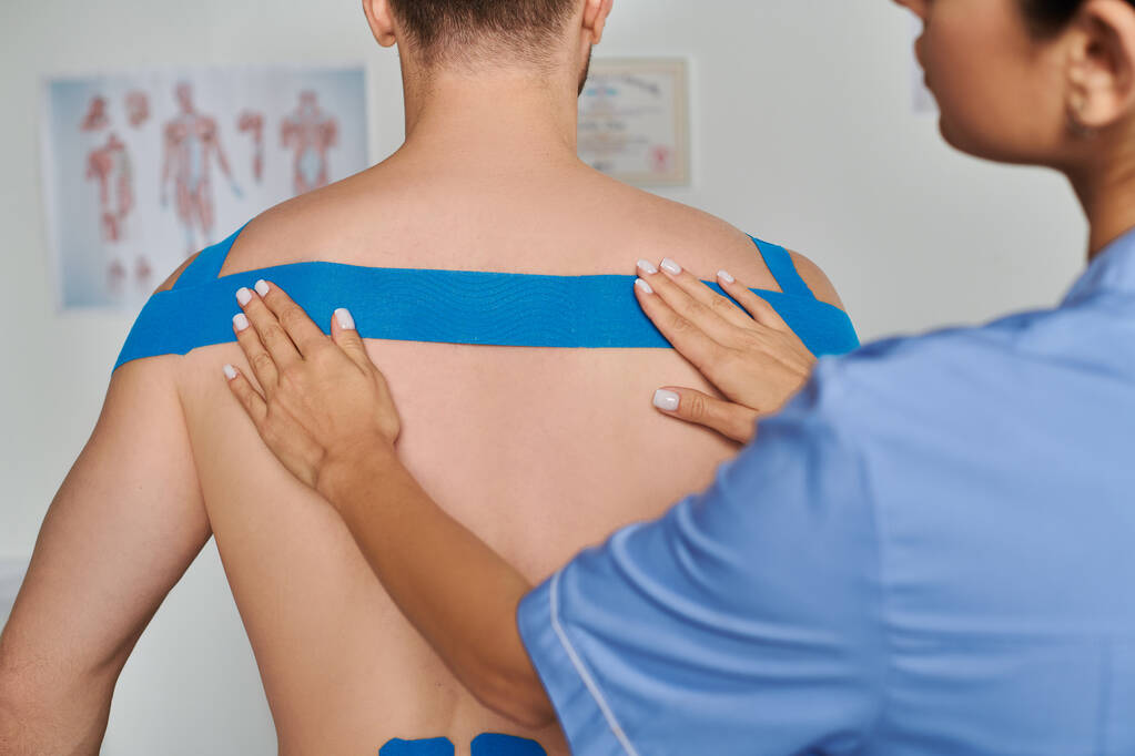 обрізаний вигляд молодої жінки-лікарки, яка кладе кінезіологічну стрічку на спину свого пацієнта, охорона здоров'я - Фото, зображення