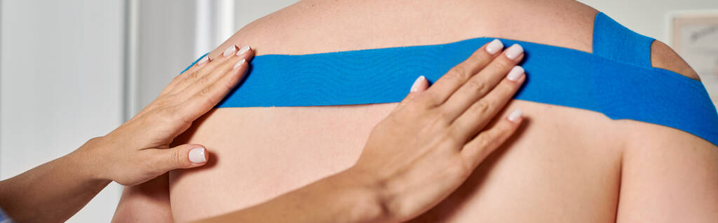 обрезанный вид рук женщины-врача, наклеивающей кинезиологическую ленту на спину своего пациента, баннер - Фото, изображение