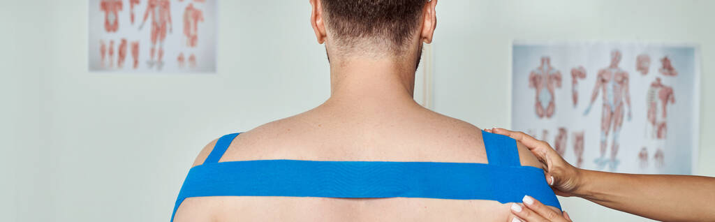 bijgesneden weergave van de hand van vrouwelijke arts zetten kinesiologische banden op het lichaam van haar patiënt, banner - Foto, afbeelding
