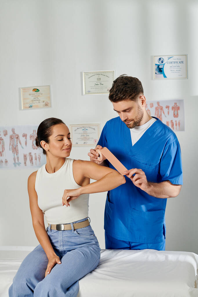 young woman in casual attire watching how doctor putting kinesio tapes on her elbow, healthcare - Photo, Image