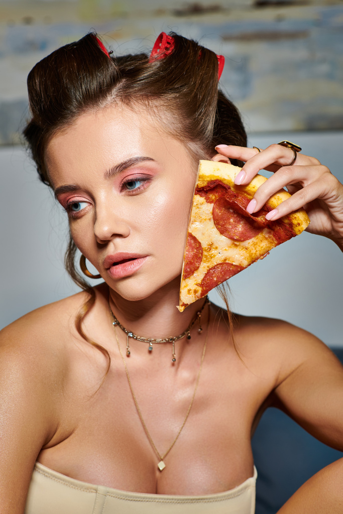 привлекательная молодая женщина с бигуди волос и аксессуаров позируя с ломтиком вкусной пиццы - Фото, изображение