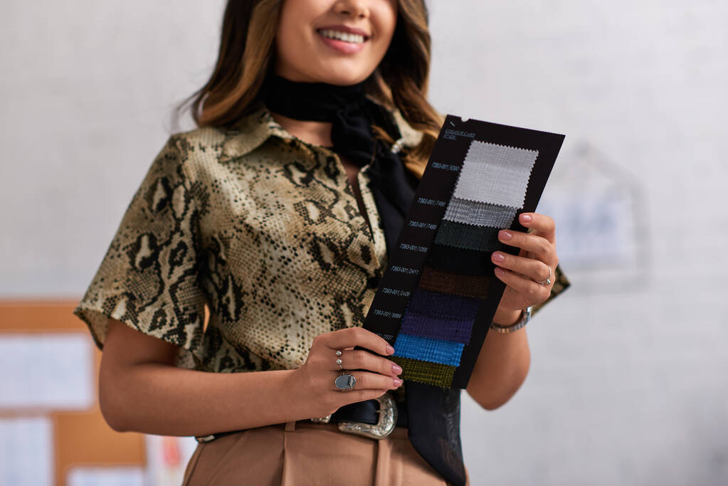 przycięty widok uśmiechniętego i stylowego projektanta trzymającego próbki kolorów w prywatnym atelier ubrań - Zdjęcie, obraz