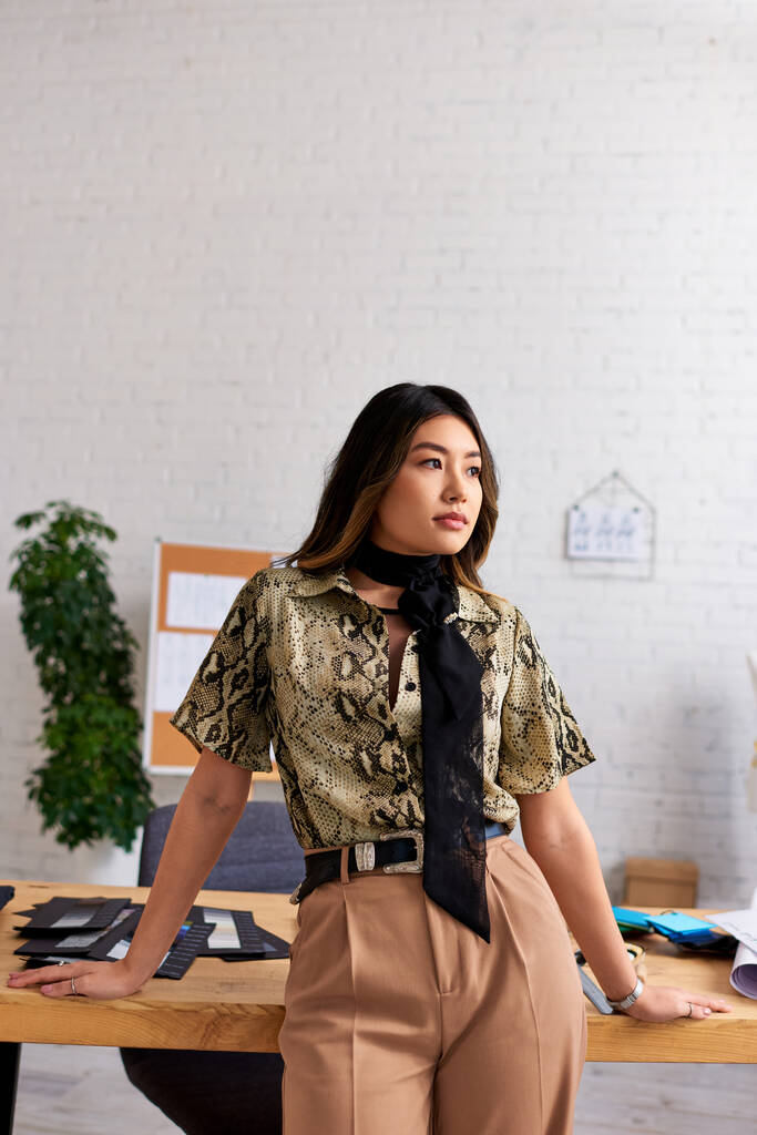 concepteur de vêtements asiatiques réfléchi regardant loin près du bureau de travail dans le studio de mode personnelle, créativité - Photo, image