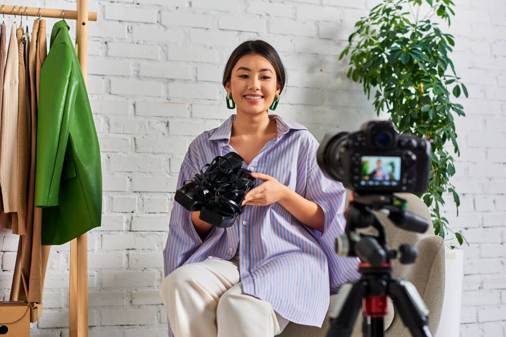 ファッションビデオブログ中にデジタルカメラの前にトレンディな靴を持つ笑顔のアジアのドレスメーカー - 写真・画像