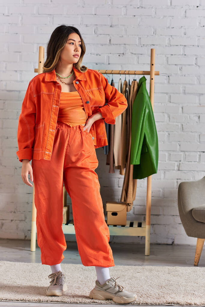 moda asiatico vestiti designer in vibrante arancione vestiti posa con le mani sul fianco in studio di moda - Foto, immagini