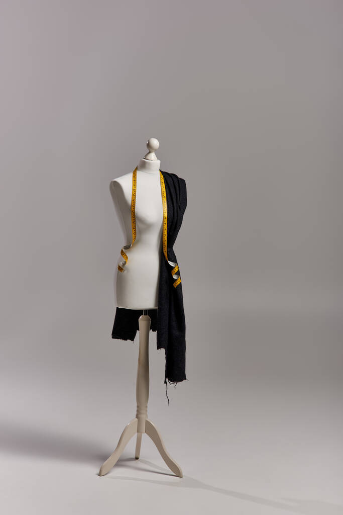 манекен на тринозі з тканиною та вимірювальною стрічкою на сірому фоні, концепція модного бізнесу - Фото, зображення