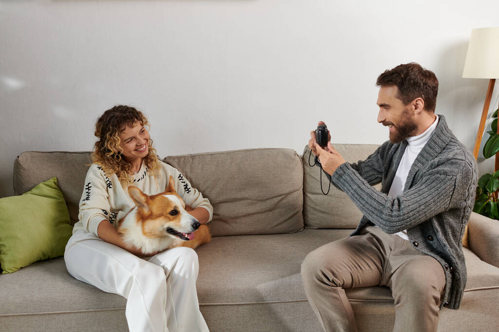 homem sorrindo e tirando foto de esposa com cachorro corgi na câmera no apartamento moderno, momentos felizes - Foto, Imagem