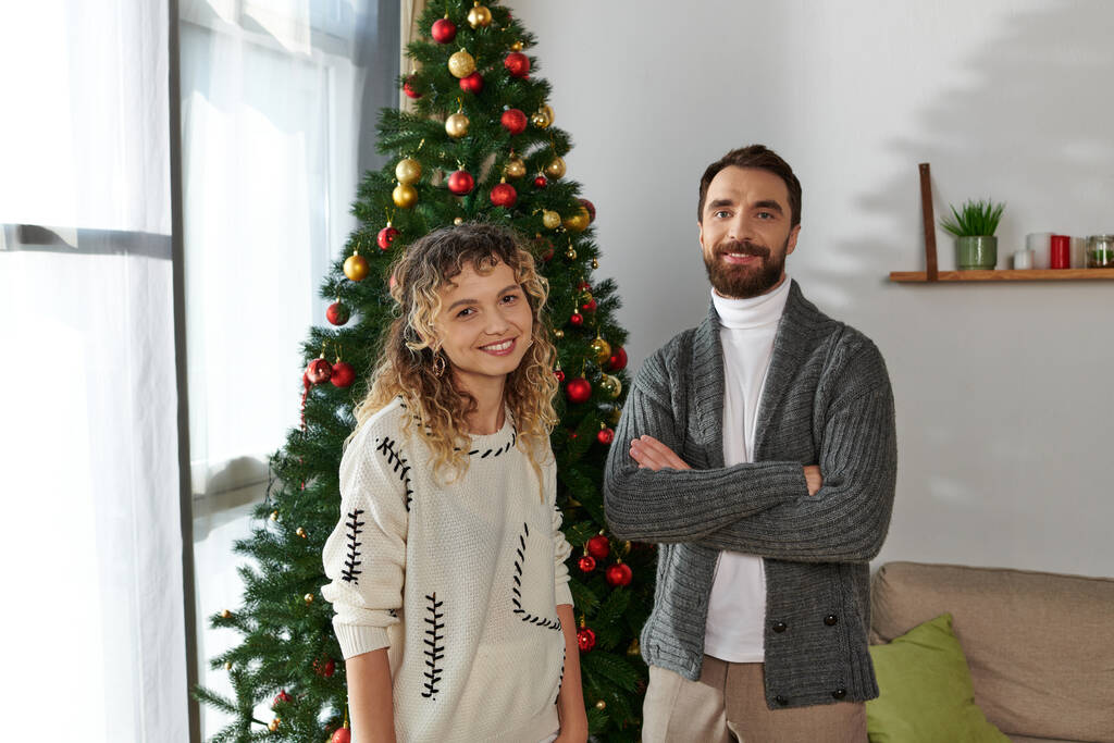 szczęśliwa para w zimie odzież stojąca w pobliżu urządzone choinki w nowoczesnym mieszkaniu - Zdjęcie, obraz