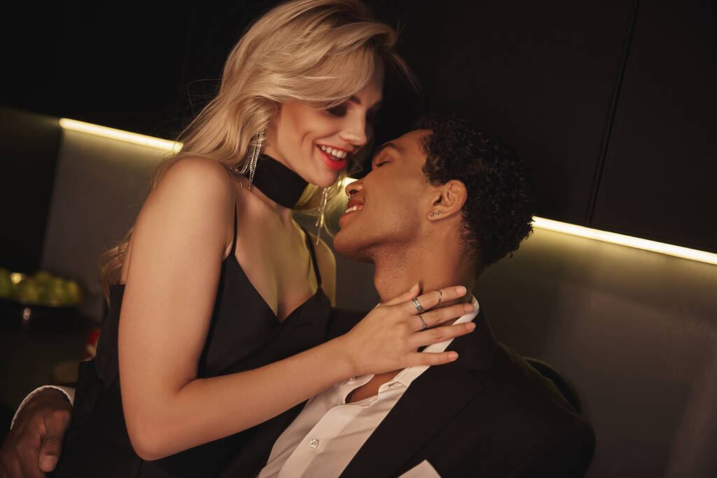 atractiva rubia alegre mujer en elegante vestido mirando amorosamente a su joven afroamericano novio - Foto, imagen