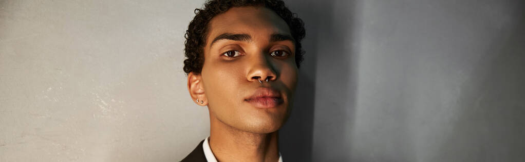 jong goed uitziende Afrikaanse Amerikaanse man in elegante pak met piercing op zoek naar camera, banner - Foto, afbeelding