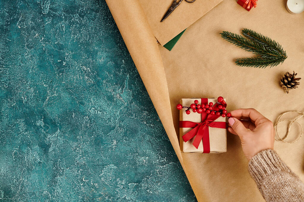 cropped view of man decorating gift box with holly berries on craft paper and blue textured backdrop - Photo, Image
