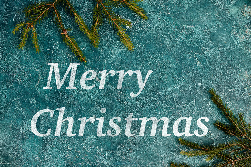 Веселі різдвяні привітання на синій сільській поверхні біля зелених гілок сосни, святковий фон - Фото, зображення