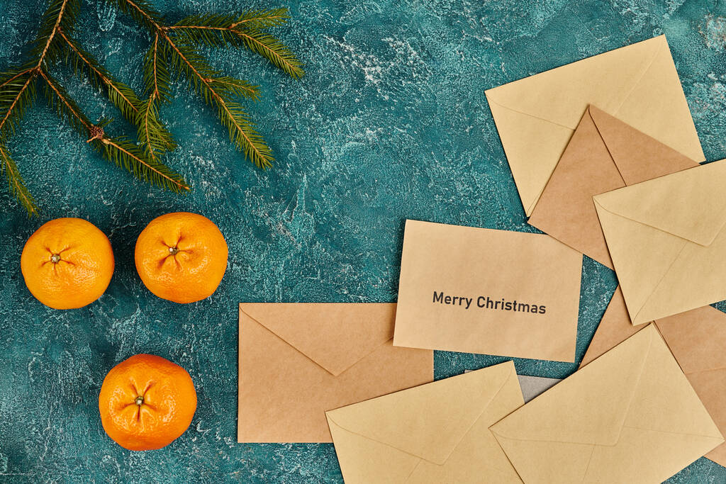 青い素朴な表面の松の枝の近くのタンジェリンおよびポスト封筒,メリークリスマスの挨拶 - 写真・画像