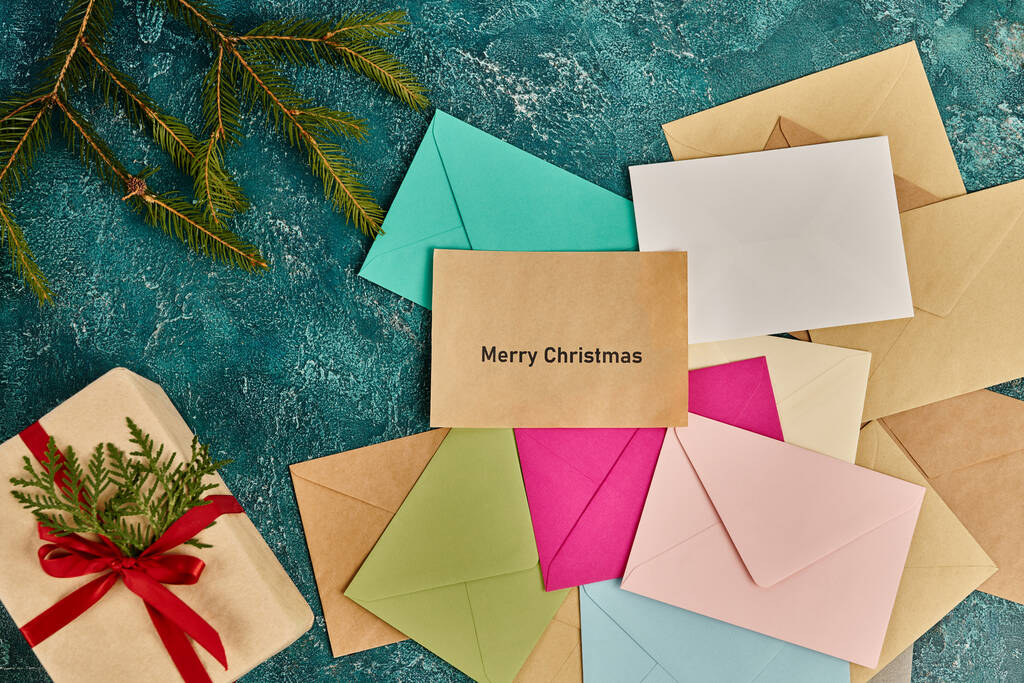 presente cerca de ramas de pino y sobres de colores sobre fondo rústico azul, letras Feliz Navidad - Foto, Imagen
