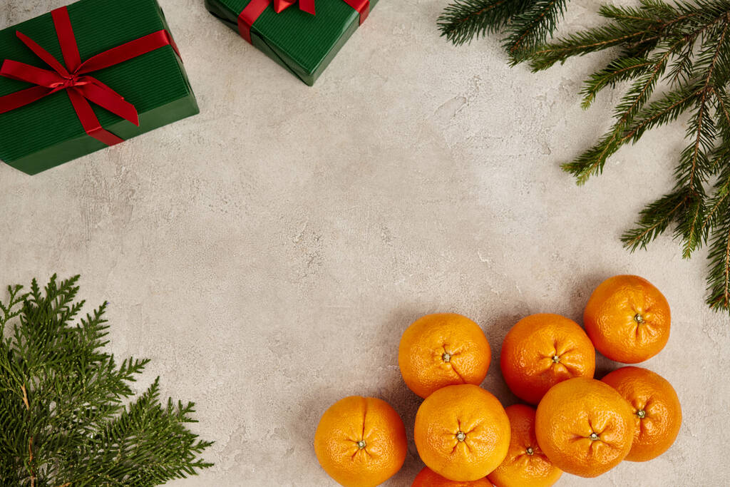 marco con mandarinas maduras y cajas de regalo verdes cerca de ramas de enebro y pino en superficie texturizada - Foto, Imagen