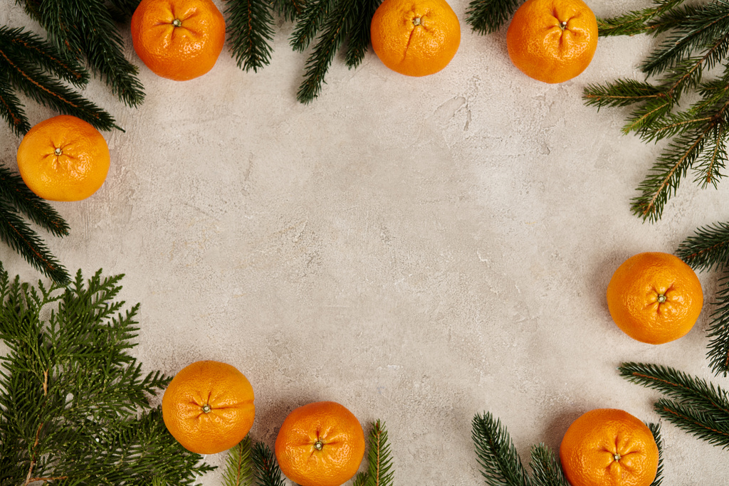 Marco de Navidad con mandarinas maduras cerca de enebro y ramas de pino sobre fondo texturizado gris - Foto, imagen