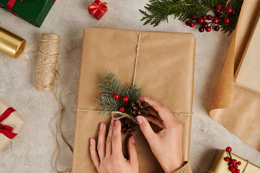 vista ritagliata di donna decorazione regalo di Natale con coni di abete e rami di pino con bacche di agrifoglio - Foto, immagini