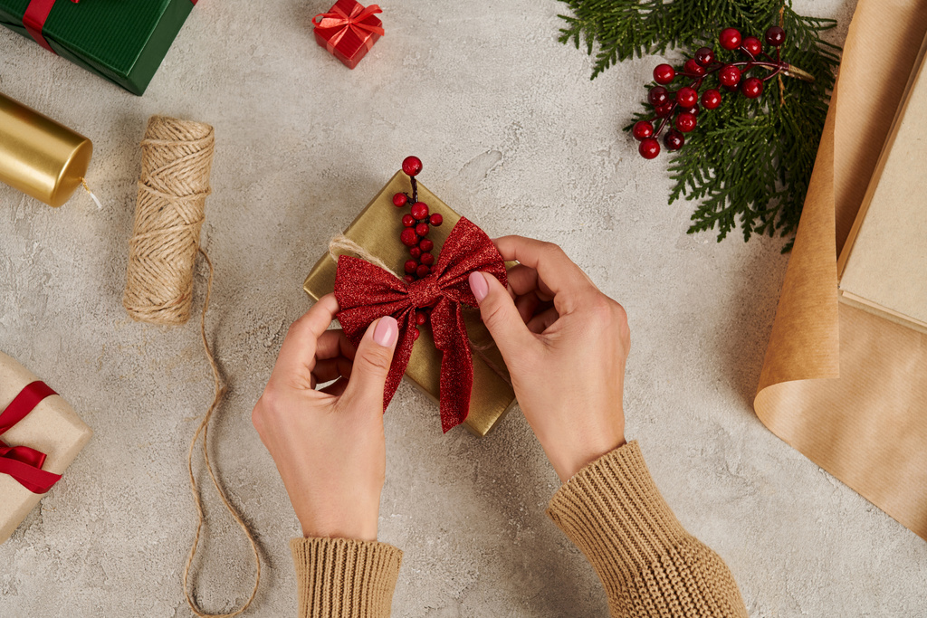 vista recortada de la mujer decorando caja de regalo con lazo rojo cerca de suministros de artesanía, telón de fondo de Navidad - Foto, imagen