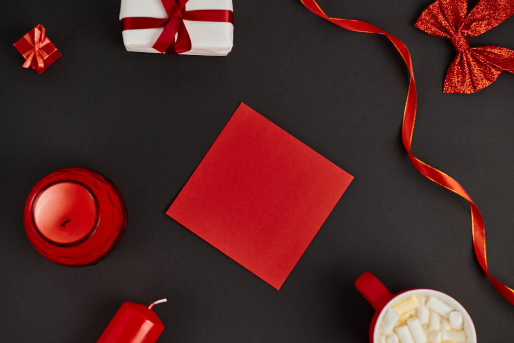 красный конверт рядом с горячим шоколадом с зефиром и красными декоративными лентами на черный, Рождество - Фото, изображение