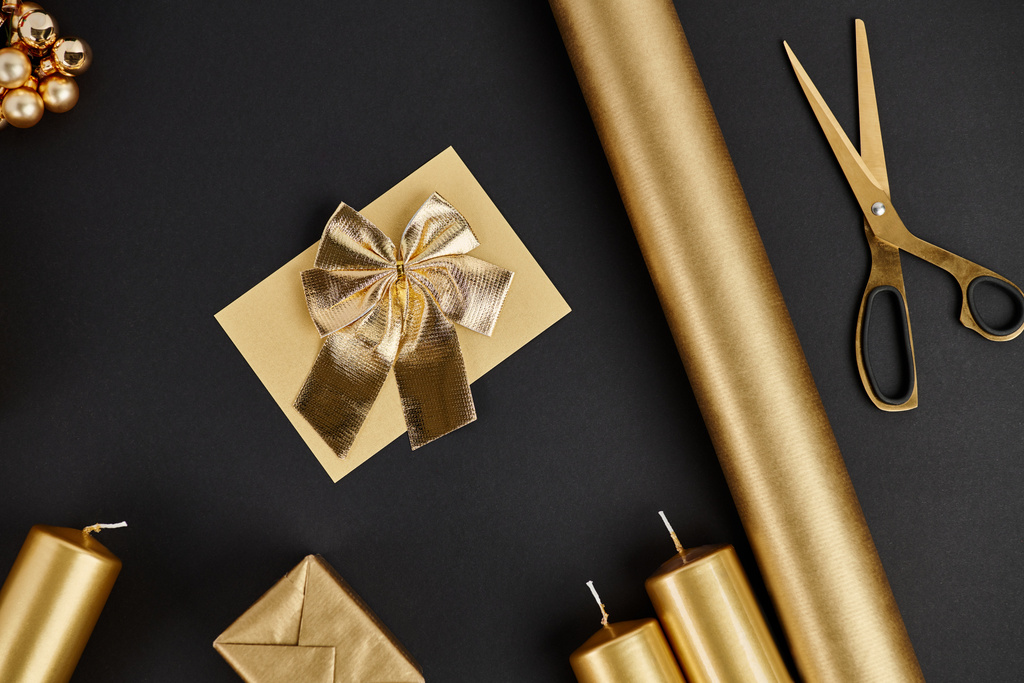 gouden kerst objecten op zwarte achtergrond, schaar in de buurt van gerold papier en kaarsen, vakantie ambachten - Foto, afbeelding